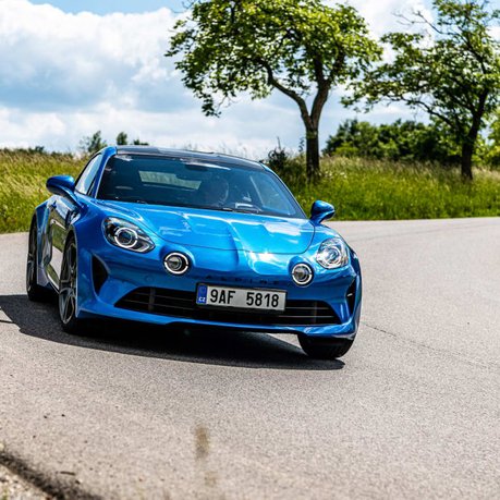 A blue Alpine A110 driving around a bend in the countryside.