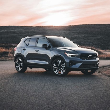 A grey Volvo XC40 with a sunset and mountains behind.