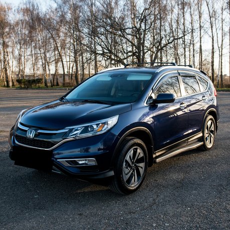 A newer style Honda CR-V parked up on a cold winters morning with trees in the background.