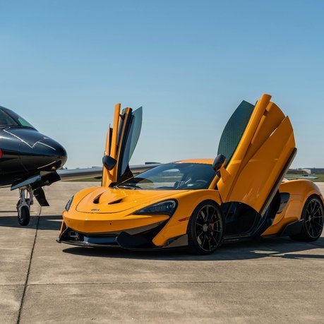 A McLaren supercar next to a fighter jet on a runway.