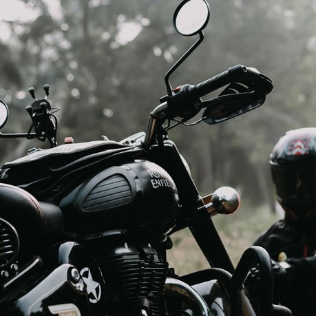 A rider in a black helmet looking at a Royal Enfield motorcycle.