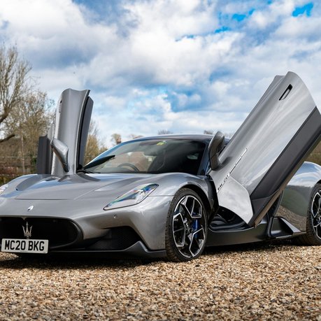 A silver Maserati on a gravel driveway, with the doors open.